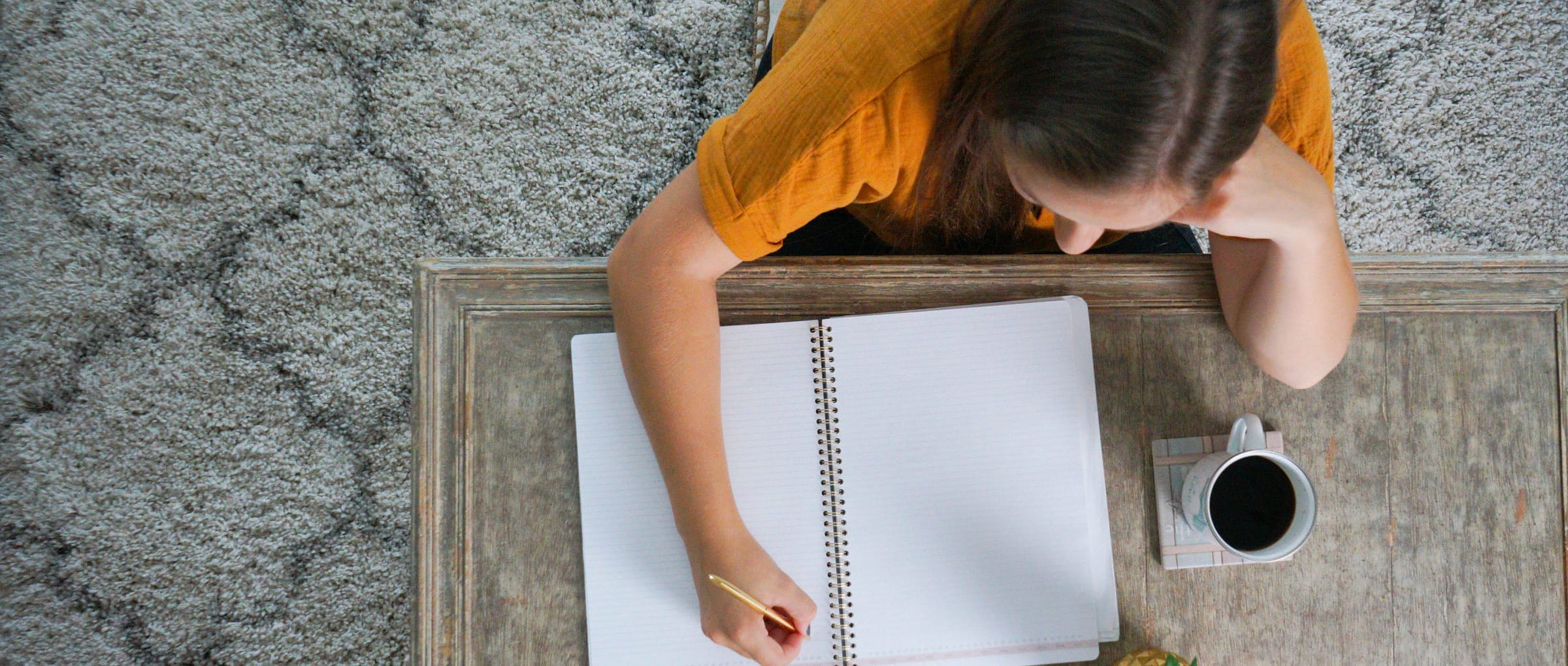 Overhead shot of Valeriya Zaytseva writing in a large notebook with a cup of coffee to the side.